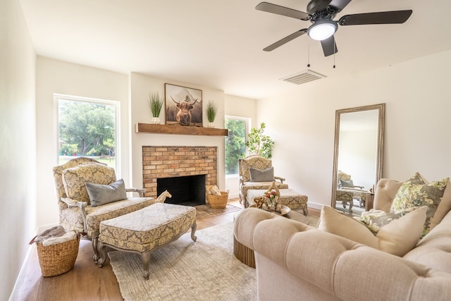 living room with a brick fireplace, ceiling fan, and light wood-type flooring