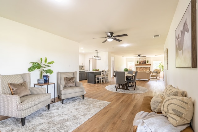 living room with ceiling fan, a fireplace, and light hardwood / wood-style flooring