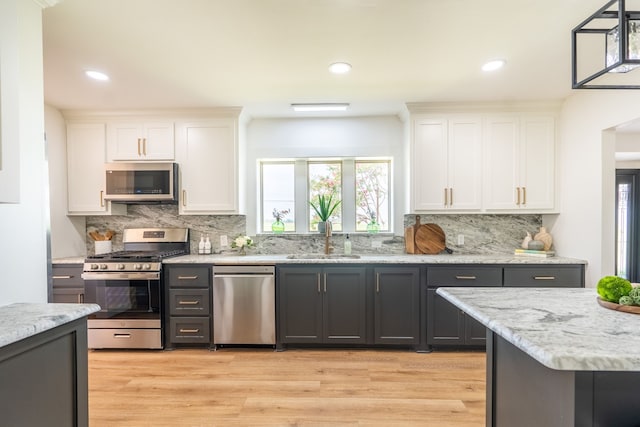 kitchen with appliances with stainless steel finishes, light stone counters, sink, white cabinets, and light hardwood / wood-style floors