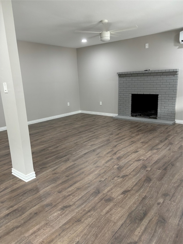 unfurnished living room with a brick fireplace, dark hardwood / wood-style flooring, ceiling fan, and a wall mounted air conditioner