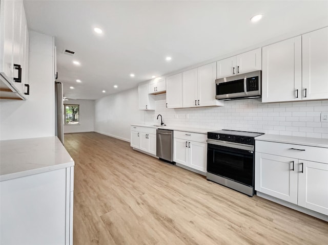 kitchen with white cabinets, appliances with stainless steel finishes, light hardwood / wood-style floors, decorative backsplash, and sink