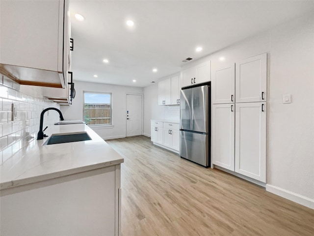 kitchen featuring white cabinets, backsplash, stainless steel fridge, and sink