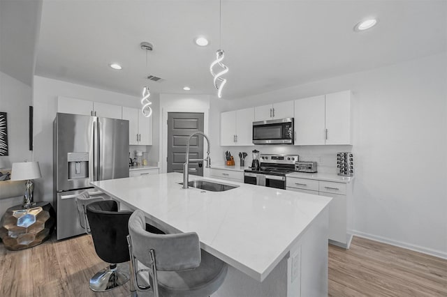 kitchen with sink, decorative light fixtures, appliances with stainless steel finishes, a kitchen island with sink, and white cabinets