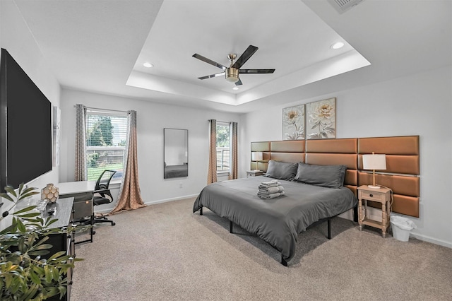 carpeted bedroom featuring a raised ceiling, ceiling fan, and multiple windows