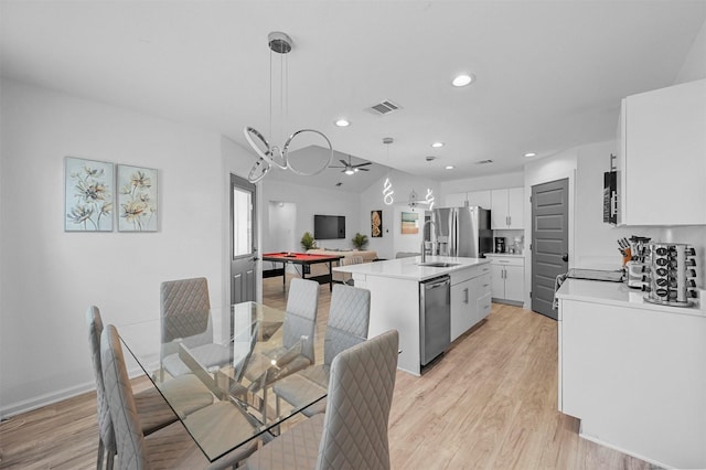 kitchen featuring appliances with stainless steel finishes, white cabinetry, a center island with sink, decorative light fixtures, and light wood-type flooring