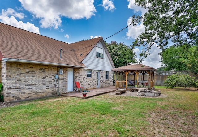 rear view of property with a wooden deck, a gazebo, an outdoor fire pit, and a lawn