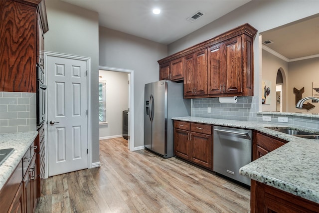 kitchen with sink, stainless steel appliances, light stone countertops, light hardwood / wood-style floors, and decorative backsplash