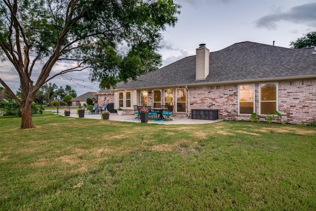 rear view of house with brick siding, a yard, a chimney, roof with shingles, and a patio area