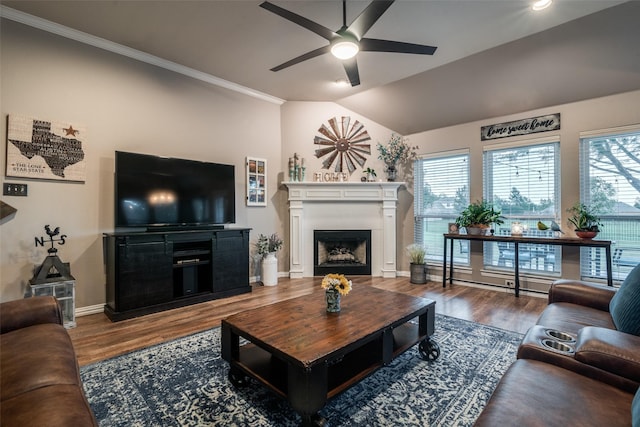 living area featuring lofted ceiling, a fireplace, wood finished floors, baseboards, and ornamental molding