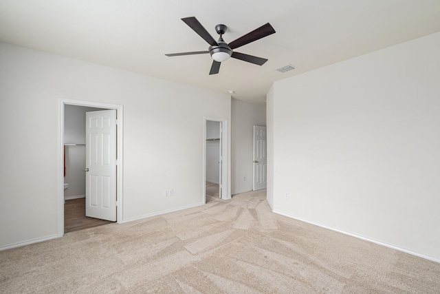 unfurnished bedroom featuring ensuite bath, light colored carpet, a walk in closet, a closet, and ceiling fan