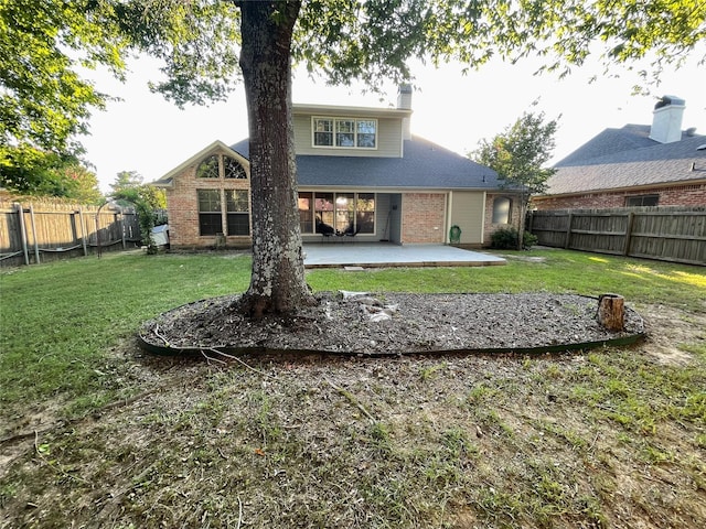 back of house with a patio, a fenced backyard, brick siding, a yard, and a chimney