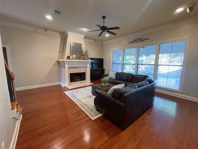 living area with baseboards, crown molding, a tiled fireplace, and wood finished floors