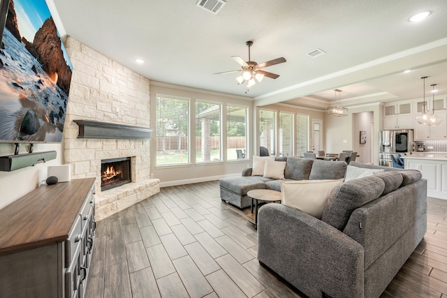 living room featuring a stone fireplace, ceiling fan, and ornamental molding