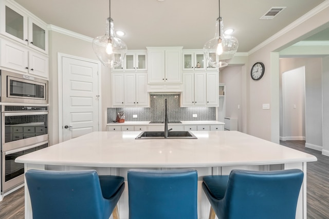 kitchen with pendant lighting, backsplash, an island with sink, appliances with stainless steel finishes, and white cabinetry