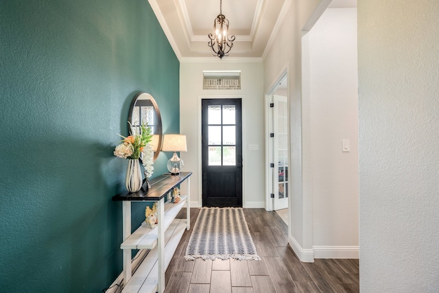 foyer with a tray ceiling, crown molding, and a chandelier