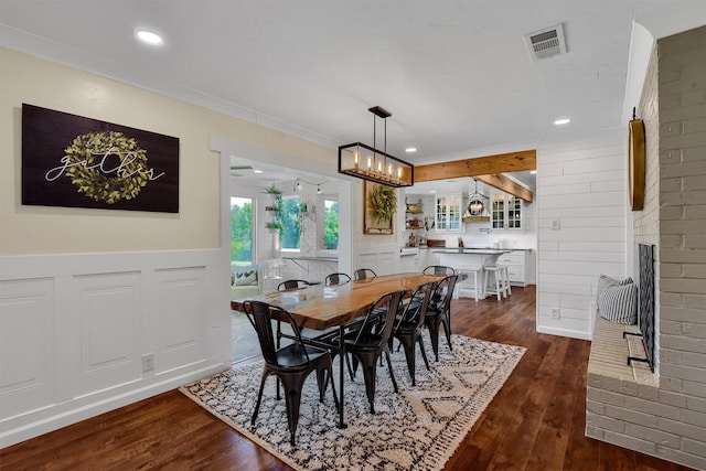 dining area with brick wall, a brick fireplace, dark hardwood / wood-style flooring, a notable chandelier, and beam ceiling