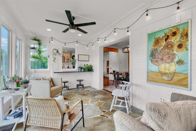 living area with brick wall, stone finish floor, and a ceiling fan