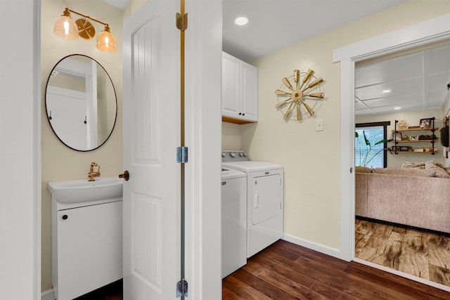 washroom with washing machine and dryer, dark wood-type flooring, a sink, baseboards, and cabinet space