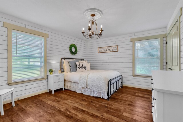 bedroom featuring a notable chandelier, dark wood-type flooring, and wood walls