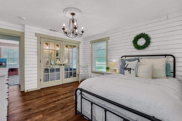 bedroom with a notable chandelier, wooden walls, french doors, and dark hardwood / wood-style floors