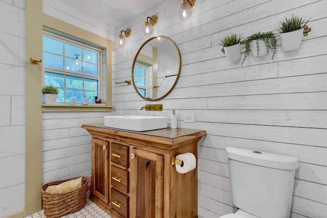 bathroom with wood walls, vanity with extensive cabinet space, toilet, and tile floors