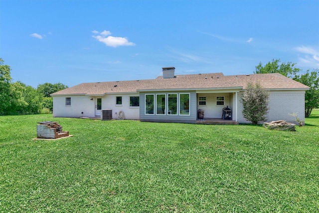 rear view of property featuring a yard, central AC unit, a shingled roof, and brick siding