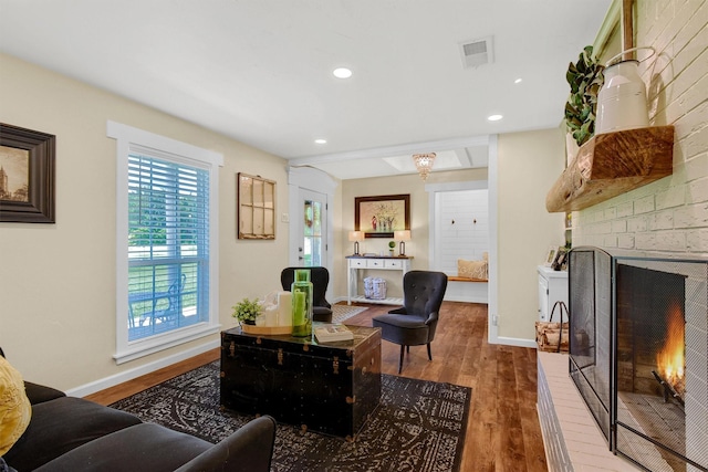 living area with a brick fireplace, baseboards, visible vents, and wood finished floors