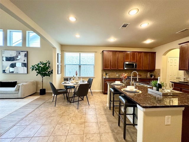 kitchen featuring a breakfast bar, sink, light tile patterned floors, dark stone countertops, and an island with sink