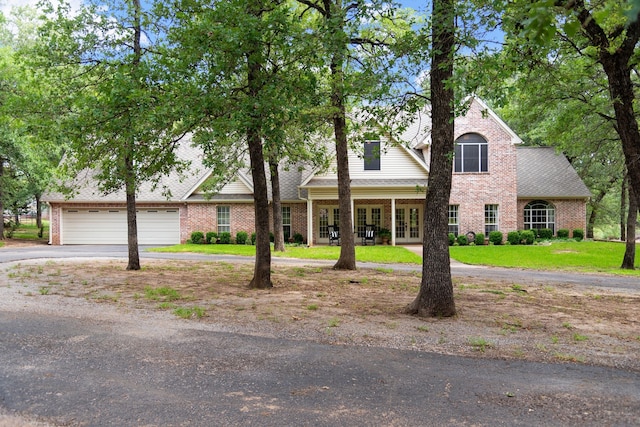 view of front of property featuring a garage, a shingled roof, brick siding, driveway, and french doors