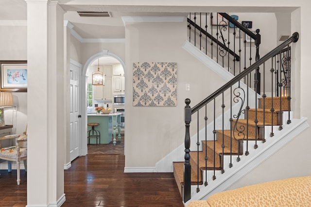 staircase with arched walkways, visible vents, baseboards, ornamental molding, and hardwood / wood-style floors