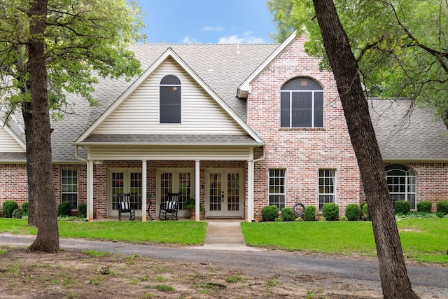 view of front of house with french doors, a shingled roof, brick siding, and a front yard