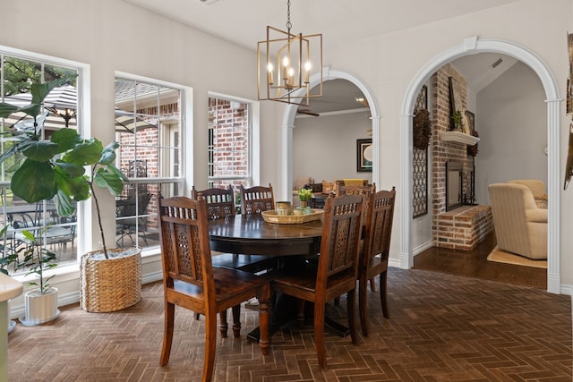 dining area with plenty of natural light, vaulted ceiling, a brick fireplace, and a notable chandelier