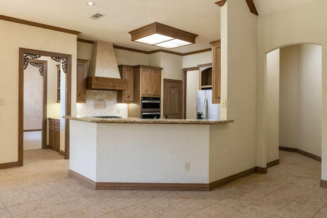 kitchen with kitchen peninsula, backsplash, light stone counters, custom range hood, and stainless steel appliances