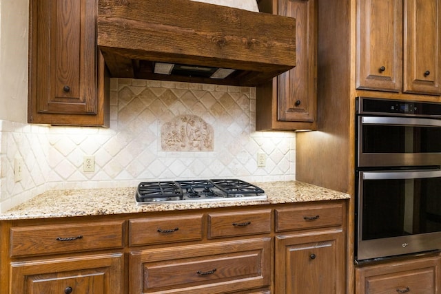 kitchen featuring backsplash, light stone countertops, stainless steel appliances, and extractor fan