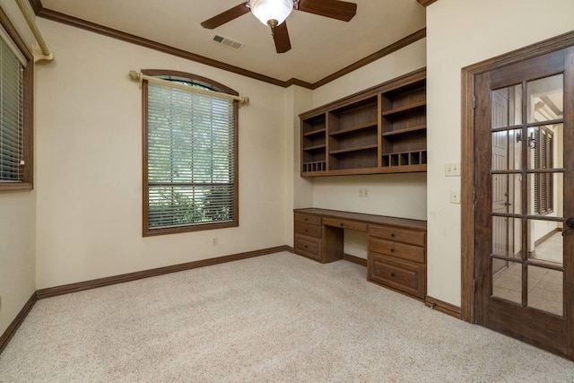 unfurnished office featuring light carpet, ceiling fan, built in desk, and ornamental molding