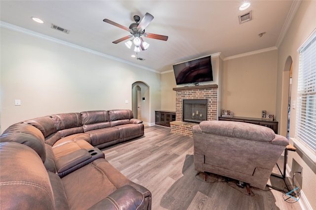 living room with a brick fireplace, ceiling fan, hardwood / wood-style flooring, and crown molding