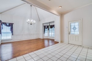 foyer entrance with a chandelier, lofted ceiling with beams, and light tile patterned floors