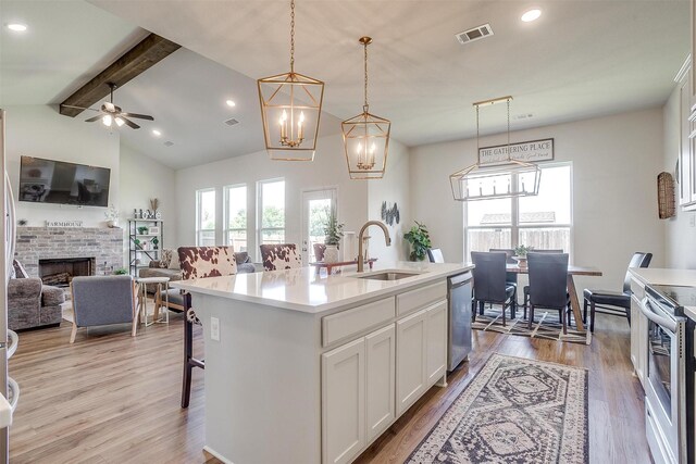 kitchen with decorative light fixtures, a fireplace, sink, appliances with stainless steel finishes, and an island with sink