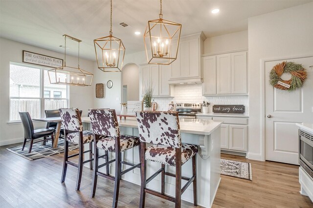 kitchen with white cabinetry, light hardwood / wood-style flooring, hanging light fixtures, and electric stove