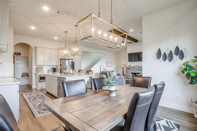 dining space featuring vaulted ceiling with beams, a brick fireplace, sink, and hardwood / wood-style flooring