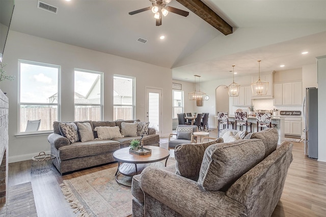 living room featuring vaulted ceiling with beams, plenty of natural light, ceiling fan with notable chandelier, and light hardwood / wood-style flooring