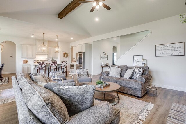 living room featuring ceiling fan with notable chandelier, dark wood-type flooring, and vaulted ceiling with beams