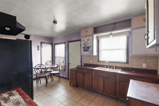 kitchen featuring backsplash, black fridge, light tile patterned floors, and sink