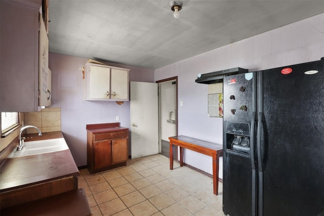 kitchen with light tile patterned flooring, black fridge with ice dispenser, and sink