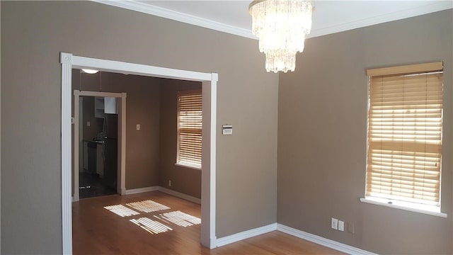 empty room featuring an inviting chandelier, hardwood / wood-style flooring, crown molding, and a wealth of natural light