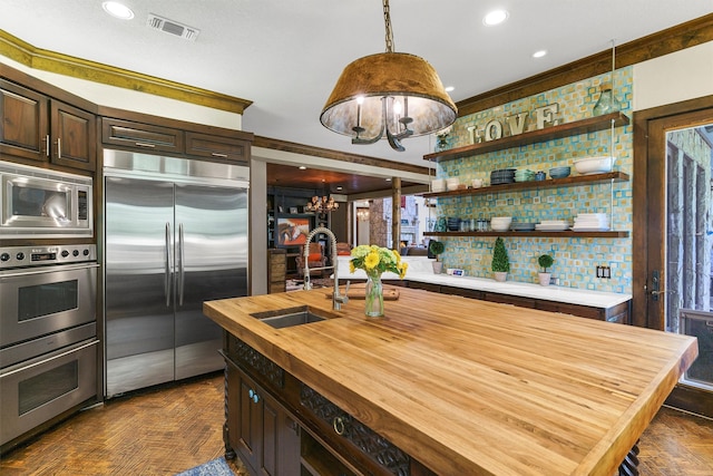 kitchen with decorative light fixtures, wooden counters, sink, built in appliances, and dark parquet floors