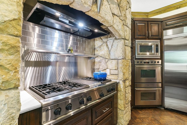 kitchen featuring ventilation hood, dark parquet floors, built in appliances, and dark brown cabinetry