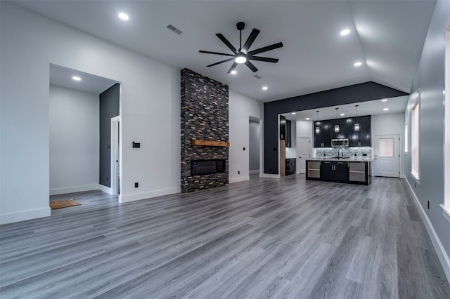 unfurnished living room featuring a fireplace, ceiling fan, hardwood / wood-style flooring, sink, and lofted ceiling