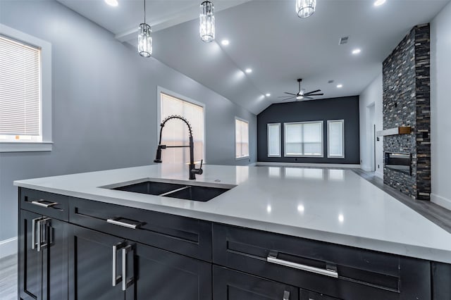 kitchen featuring decorative light fixtures, ceiling fan, a stone fireplace, wood-type flooring, and sink