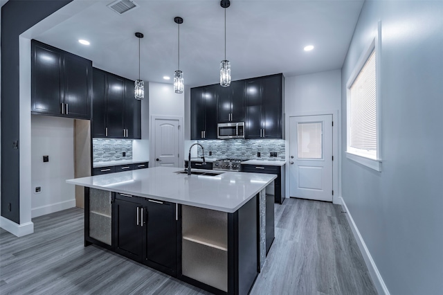 kitchen with light hardwood / wood-style floors, stainless steel appliances, decorative light fixtures, backsplash, and sink